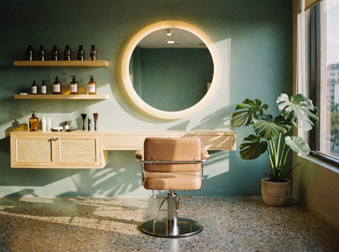 A bright, calm salon in Makati in late-afternoon light — one styling chair at a round mirror, plants by the window