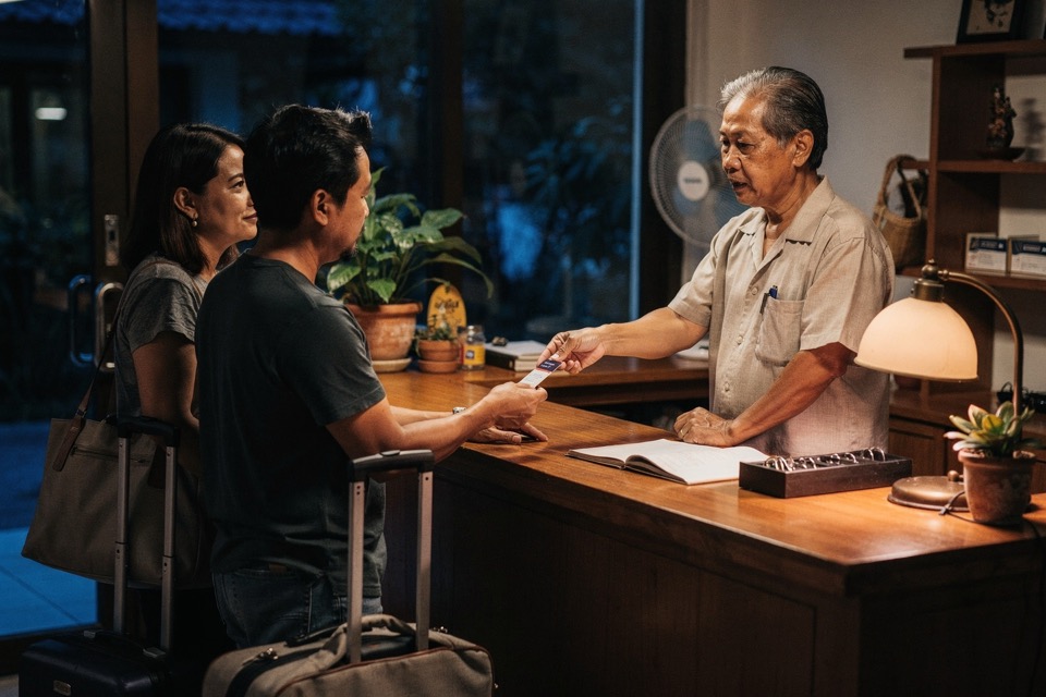 Night hotel staff member welcoming arriving guests and handing over a room key at reception