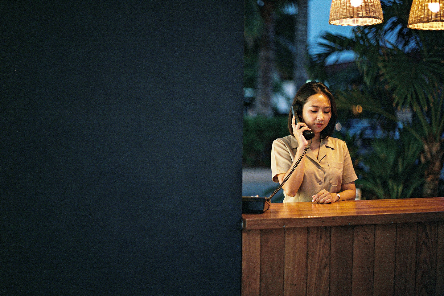 A hotel receptionist answering the telephone at a warm independent hotel reception desk after dark